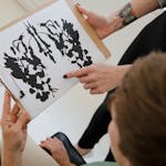Hands holding a clipboard with an inkblot for psychological analysis.